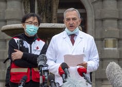 Two men, one in a mask, stand together.