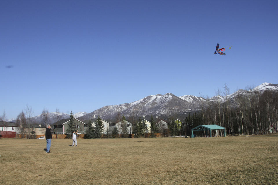 This March 3, 2019, photo shows 10-year-old Daniel Hansell, right, and his father, Jeff Hansell, flying a kite in a park in East Anchorage, Alaska, with the snow-covered Chugach Mountains in the background. Much of Anchorage's snow disappeared as Alaska experienced unseasonably warm weather in March. (AP Photo/Mark Thiessen)