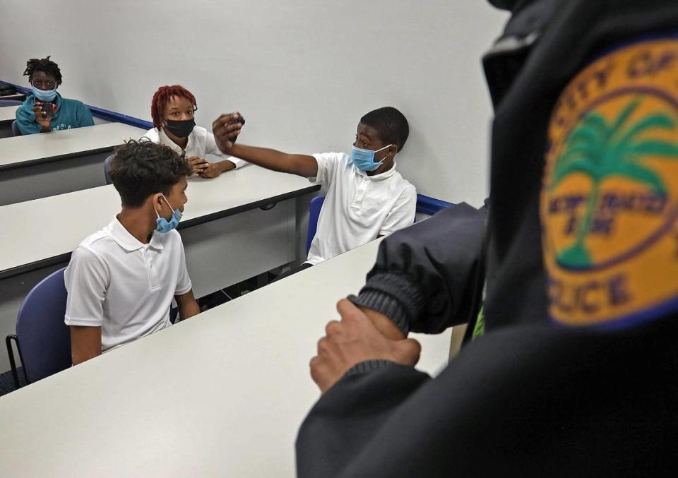 Victor Cochez, 14, left, and Tacora Bryan, 16, watch as Tyquane Hankerson, 14, attempts to start the body camera during a presentation by Miami Police.