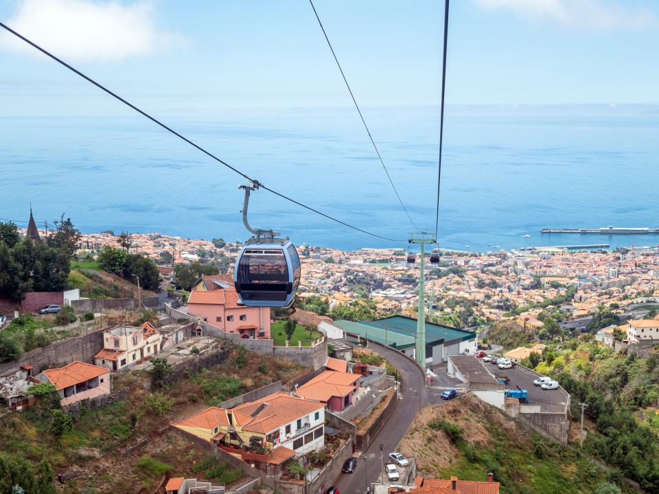 A blue cable car over buildings going toward the ocean.