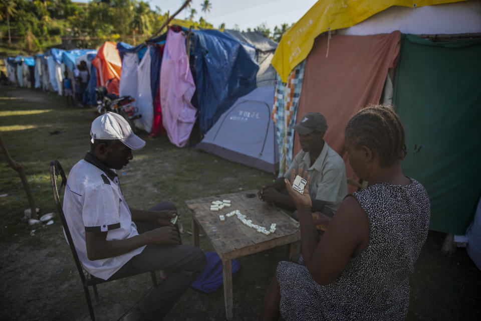 Refugees play dominoes next to their makeshift tents at the Devirel camp, six months after 7.2 magnitude earthquake in Les Cayes, Haiti, Wednesday, Feb. 16, 2022. Thousands of Haitians who lost their homes in the quake remain in camps, living in cramped shelters made of plastic and cloth sheets and corrugated metal. (AP Photo/ Odelyn Joseph)