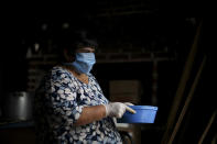 La voluntaria Leonor Esquivel, con una mascarilla protectora y guantes desechables, sostiene un recipiente lleno de guiso de lentejas afuera de un comedor popular en las afueras de Buenos Aires, Argentina, el miércoles 25 de marzo de 2020. (AP Foto / Natacha Pisarenko)