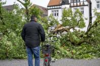A man stands in front of a fallen tree in the town hall square of Lippstadt, Germany, a day after heavy rains and storms hit the area, Saturday, May 21, 2022. (David Inderlied/dpa via AP)