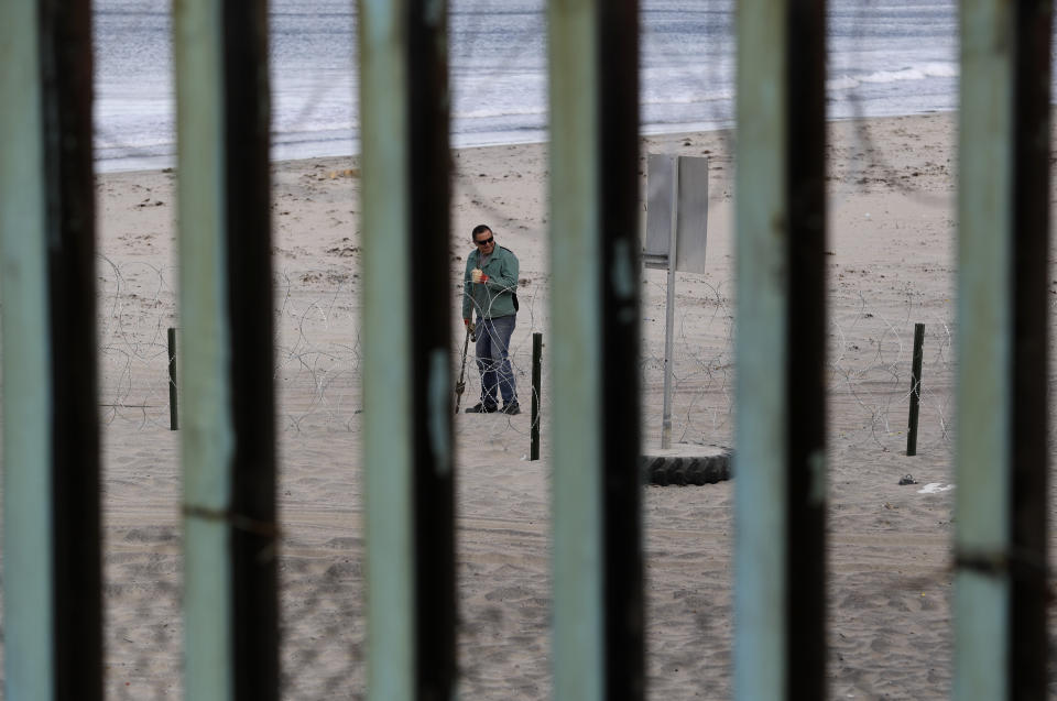 Un trabajador instala alambre de concertina en el lado estadounidense de la frontera, visto a través de las barras de la estructura fronteriza en Tijuana, México, el miércoles 14 de noviembre de 2018. (AP Foto/Gregory Bull)