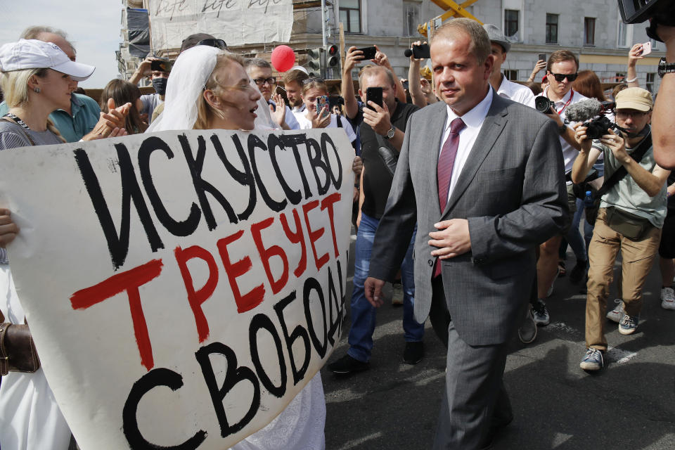 Yuri Bondar, Belarusian Minister of Culture, passes a woman holding a banner reading "Art demands freedom" in Minsk, Belarus, Tuesday, Aug. 18, 2020. Several dozen people gathered in front of the theater to support the troupe that handed in their notice to quit after the theater's director, Pavel Latushko, was fired. (AP Photo/Dmitri Lovetsky)