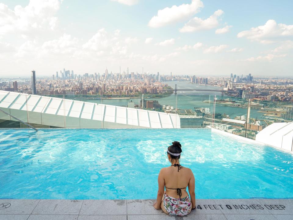 The author sits on the edge of the pool facing the NYC skyline in the background.