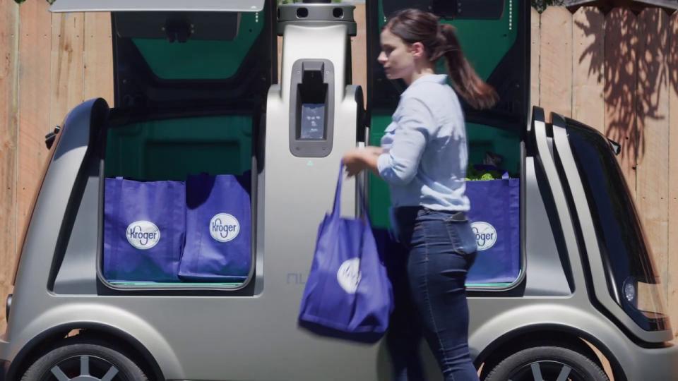 A woman removes Kroger groceries from a self-driving vehicle.