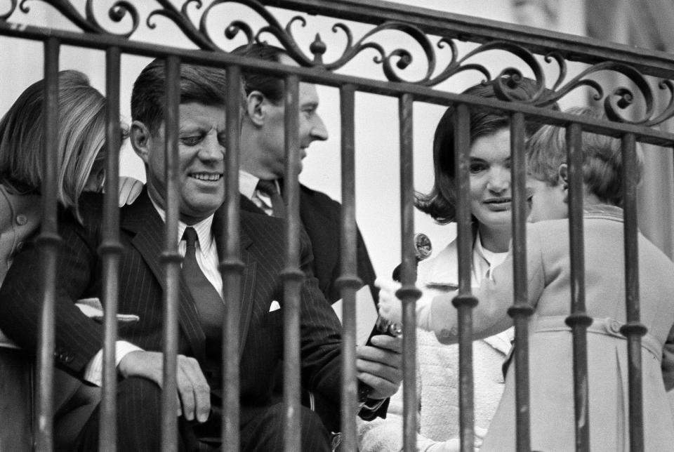 FILE - In this Nov. 13, 1963 file photo, U.S. President John F. Kennedy and first lady Jacqueline Kennedy sit with their children, John Jr. and Caroline, on a portico overlooking the White House South Lawn in Washington. In background is British Ambassador David Ormsby Gore. (AP Photo)