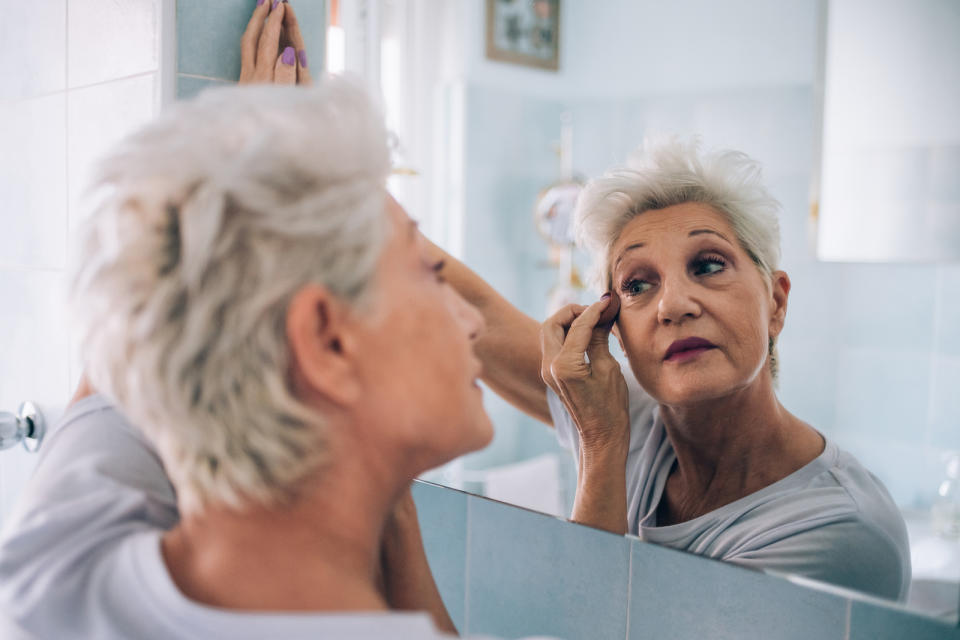 Senior woman looking in mirror, applying makeup