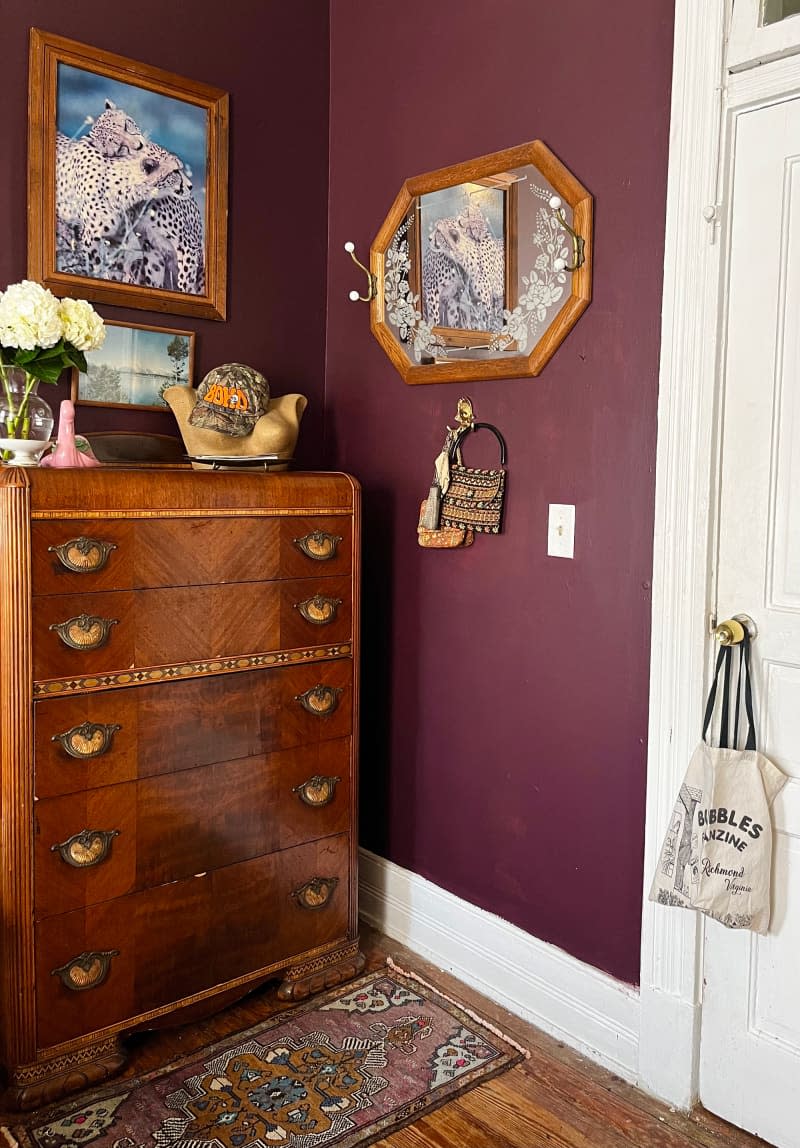 Wood dresser in corner of eggplant bedroom.