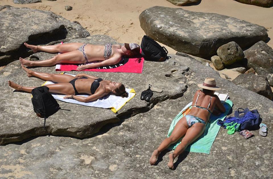 Three women in bikinis sunbathe on rocks at Bondi.