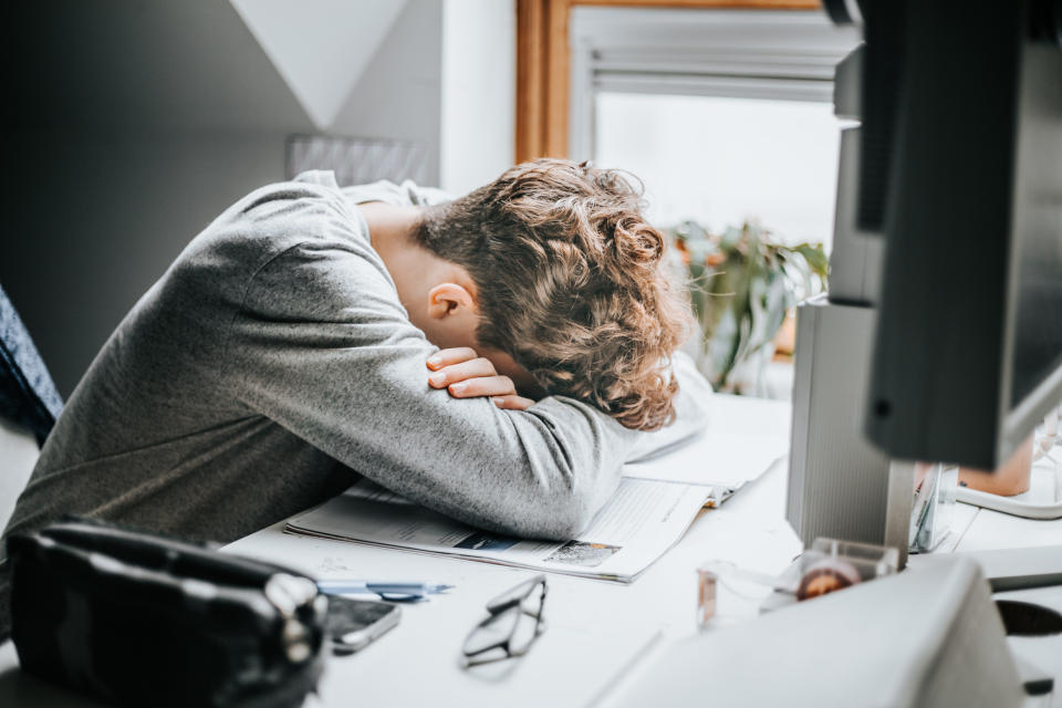 Person resting head on arms at a desk with computer screen, indicating fatigue or stress