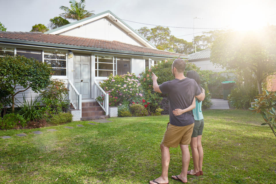 A couple stands in front of a house while looking to buy a home.