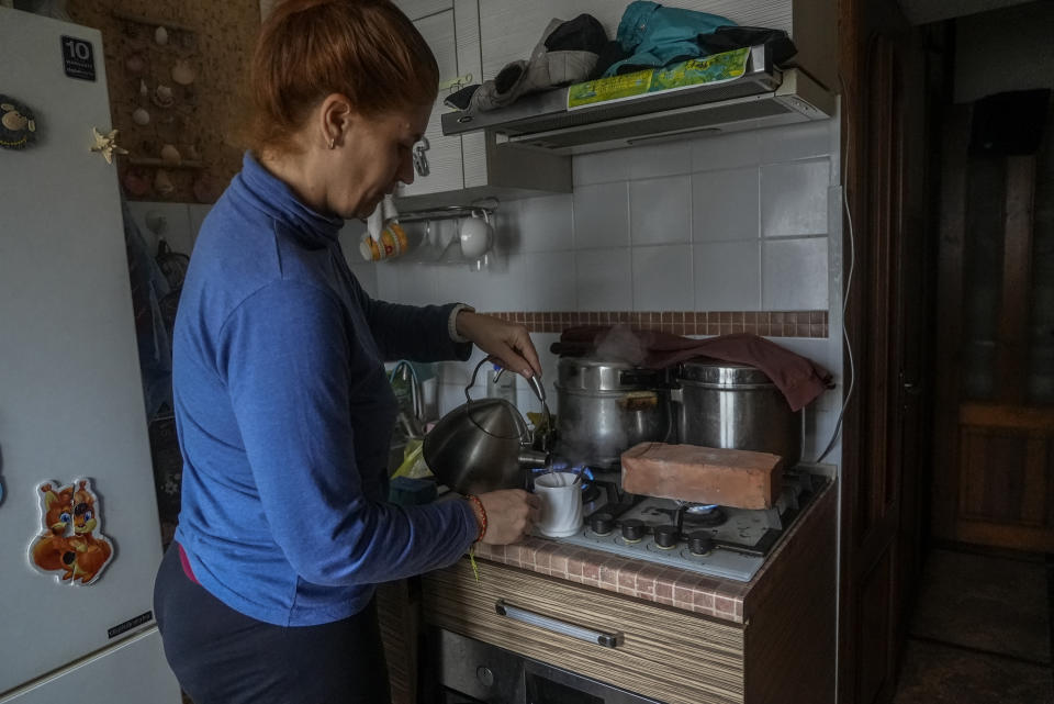 Larysa Shevtsova pours a cup of tea in her kitchen in Kherson, Ukraine, while a fire-resistant brick heats on the stove on Nov. 26, 2022. When the rectangular block was hot enough, it was carried carefully into the living room and set on top of a Soviet-era space heater that no longer worked. Shevtsova, her husband and two sons, one of them three years old, huddled around the brick for warmth that would last for about 30 minutes. “We use this method to heat the room,” Shevtsova said. “Before that we just froze.” (AP Photo/Sam Mednick)