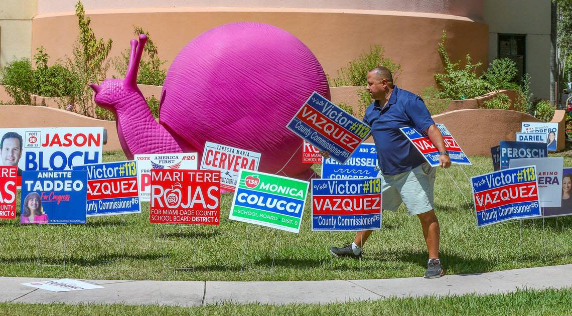 Campaign manager Mario Catalino carries campaign signs for county commissioner candidate Victor Vazquez in front of the pink snail sculpture at Precinct 609 at the Coral Gables War Memorial Youth Center on Tuesday, August 23, 2022.