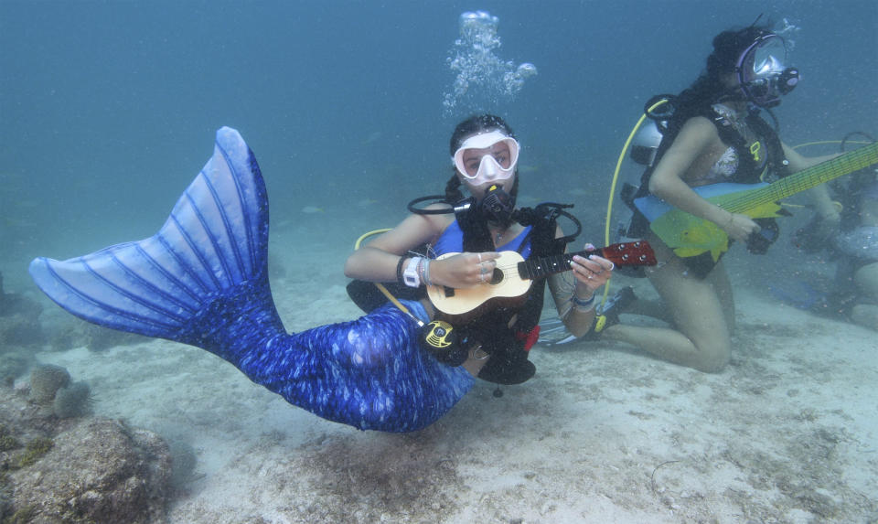 In this photo provided by the Florida Keys News Bureau, Tamara Bredova, left, costumed as a mermaid, pretends to play a ukulele underwater, Saturday, July 8, 2023, while Kelly Angel, right, strokes a faux guitar at the Lower Keys Underwater Music Festival in the Florida Keys National Marine Sanctuary near Big Pine Key, Fla. Several hundred divers and snorkelers submerged along a portion of the continental United States' only living coral barrier reef to listen to a local radio station's four-hour broadcast, piped beneath the sea to promote coral reef preservation. Kelly Angel is at right. (Frazier Nivens/Florida Keys News Bureau via AP)