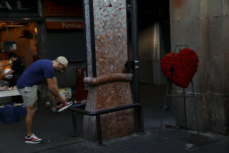 A man ties his shoe next to a wreath at the entrance to La Boqueria market, near the area where a van crashed into pedestrians at Las Ramblas in Barcelona, Spain August 21, 2017. REUTERS/Susana Vera