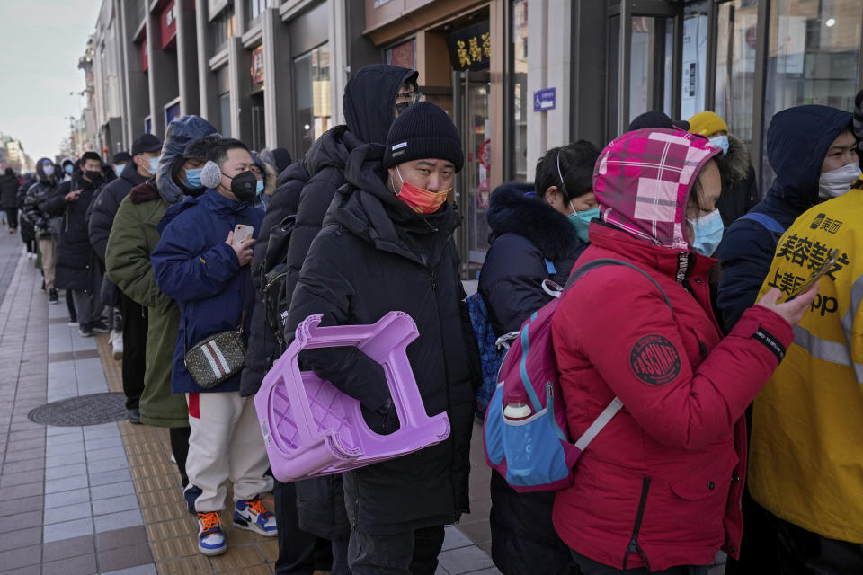 A man carries a plastic chair as he and hundreds of residents line up to visit a store selling 2022 Winter Olympics memorabilia in Beijing, Monday, Feb. 7, 2022. The race is on to snap up scarce 2022 Winter Olympics souvenirs. Dolls of mascot Bing Dwen Dwen, a panda in a winter coat, sold out after buyers waited in line overnight in freezing weather. (AP Photo/Andy Wong)