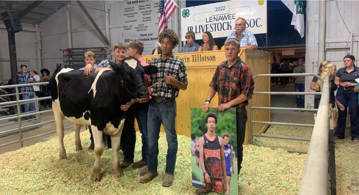 Zachariah Stephens, older brother of the late Isiah Stephens, is pictured at one of the 4-H auctions at the 2022 Lenawee County Fair with Isiah's market Holstein and Isiah's best friend, Lucas Morse, holding the photo of Isiah, as well as, from left, Ashton Platt, Hailey Bennett (out of view), Trevor Lakatos and Carter Kiel. Several thousand dollars were raised in Isiah's memory at the auction.