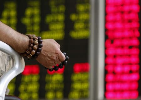 FILE PHOTO: An investor holds onto prayer beads as he watches a board showing stock prices at a brokerage office in Beijing, China, July 6, 2015. REUTERS/Kim Kyung-Hoon/File Photo