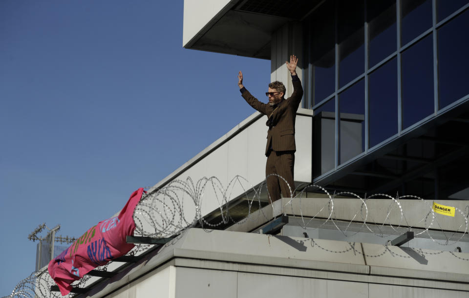 An Extinction Rebellion demonstrator gestures with a banner as he occupies a raised area at City Airport in London, Thursday, Oct. 10, 2019. Some hundreds of climate change activists are in London during a fourth day of world protests by the Extinction Rebellion movement to demand more urgent actions to counter global warming. (AP Photo/Matt Dunham)