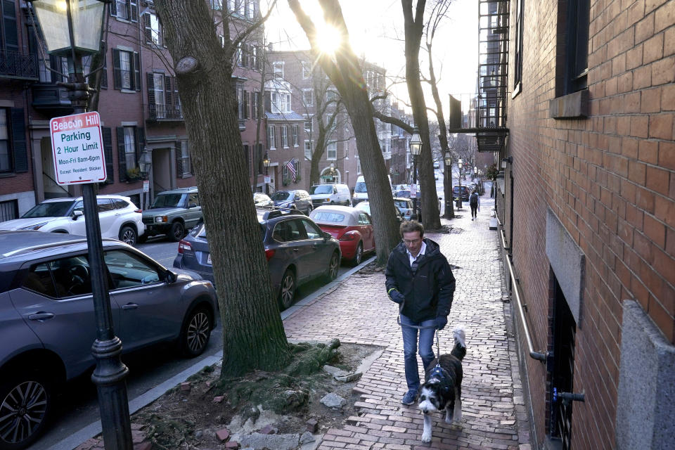 A passer-by walks their dog in a residential area near the Statehouse on Beacon Hill, Monday, Feb. 13, 2023, in Boston. For much of the Eastern United States, the winter of 2023 has been a bust. Snow totals are far below average from Boston to Philadelphia in 2023 and warmer temperatures have often resulted in more spring-like days than blizzard-like conditions. (AP Photo/Steven Senne)