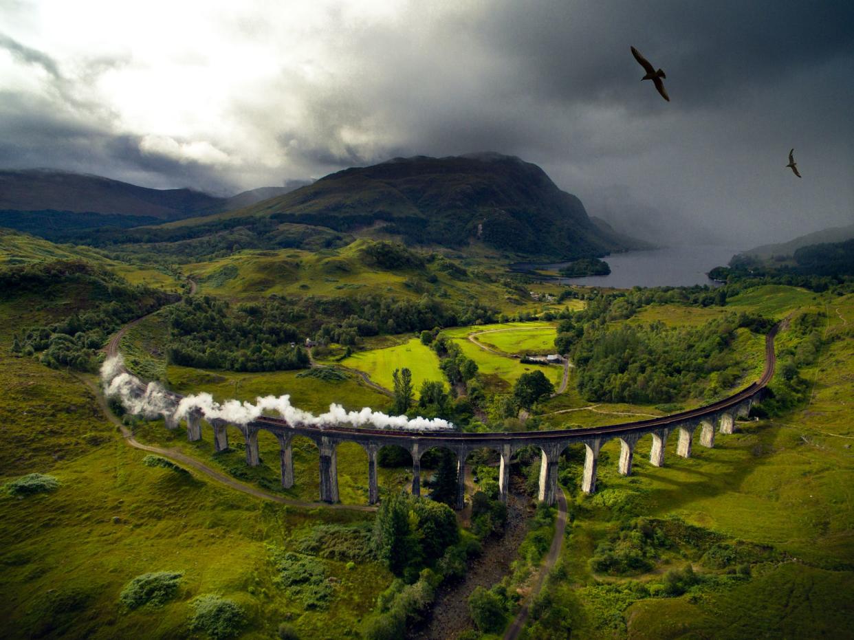 Train along Glenfinnan Viaduct, Inverness-shire, Scotland, grey clouds with birds flying over