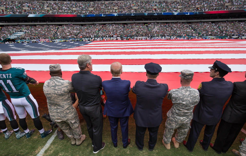 Vice President Joe Biden (blue suit),&nbsp;Philadelphia Eagles head coach Doug Pederson (left), and members of the military and police help hold a large American flag before a 2016 game. (Photo: USA Today Sports / Reuters)
