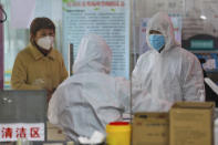 Medical workers in protective gear talk with a woman suspected of being ill with a coronavirus at a community health station in Wuhan in central China's Hubei Province, Monday, Jan. 27, 2020. China on Monday expanded sweeping efforts to contain a viral disease by extending the Lunar New Year holiday to keep the public at home and avoid spreading infection. (Chinatopix via AP)