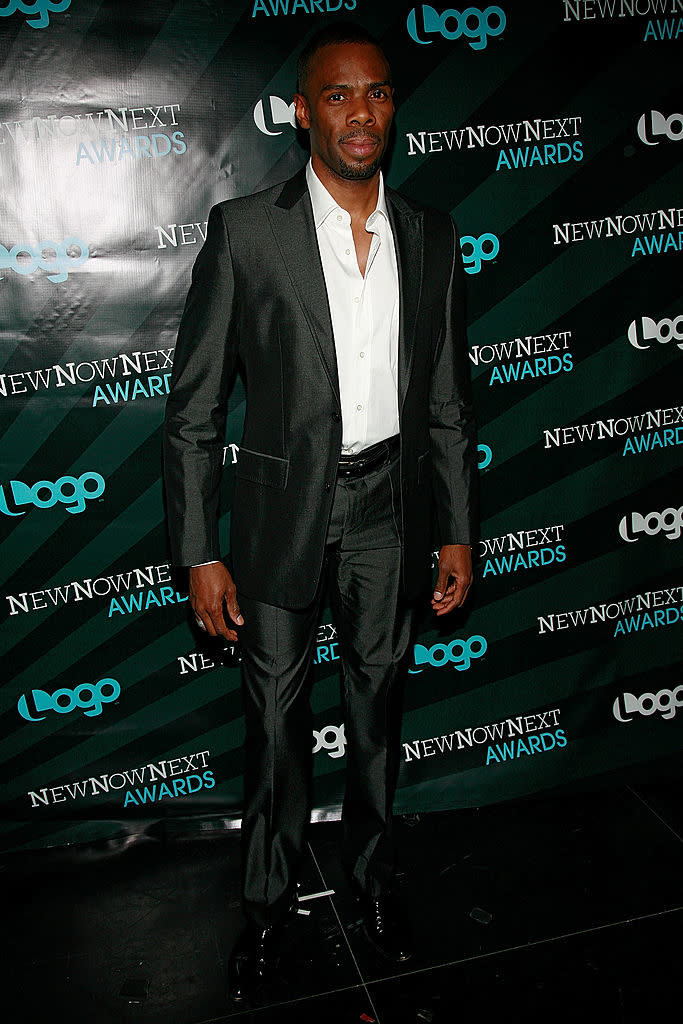 Man in a black suit and dress shoes posing at an event with backdrop featuring 'Logo NewNowNext Awards'