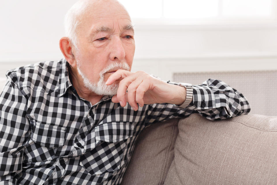 Older man sitting on couch, with hand resting on chin as if deep in thought.