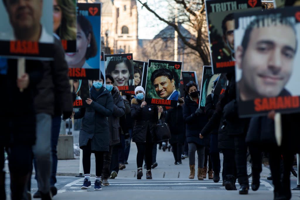 People hold signs with images of the victims of the downed Ukraine International Airlines Flight 752, as family and friends gather to take part in a march to mark the first anniversary, in Toronto on January 8, 2021.