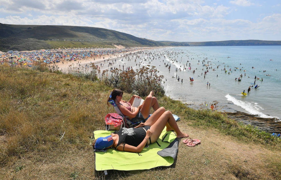 People sunbath on the clifftop at Woolacombe Beach in North Devon as another spell of warm weather hits the UK.