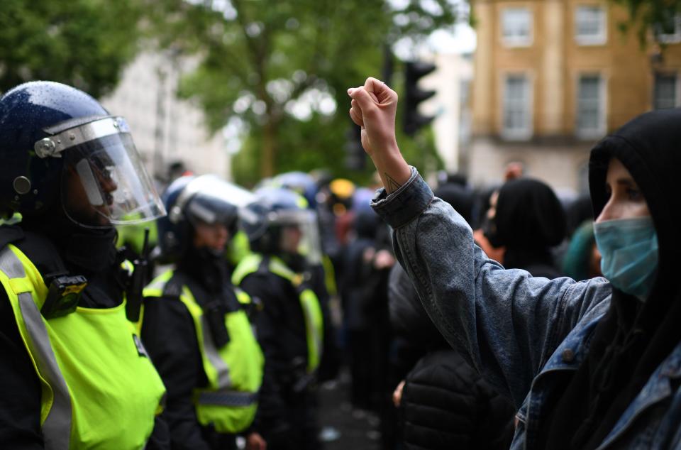 A protester (R) wearing PPE (personal protective equipment), including a face mask as a precautionary measure against COVID-19, makes a fist as she stands by Police officers in riot in central London on June 6, 2020, during a demonstration organised to show solidarity with the Black Lives Matter movement in the wake of the killing of George Floyd, an unarmed black man who died after a police officer knelt on his neck in Minneapolis. - The United States braced Friday for massive weekend protests against racism and police brutality, as outrage soared over the latest law enforcement abuses against demonstrators that were caught on camera. With protests over last week's police killing of George Floyd, an unarmed black man, surging into a second weekend, President Donald Trump sparked fresh controversy by saying it was a "great day" for Floyd. (Photo by DANIEL LEAL-OLIVAS / AFP) (Photo by DANIEL LEAL-OLIVAS/AFP via Getty Images)