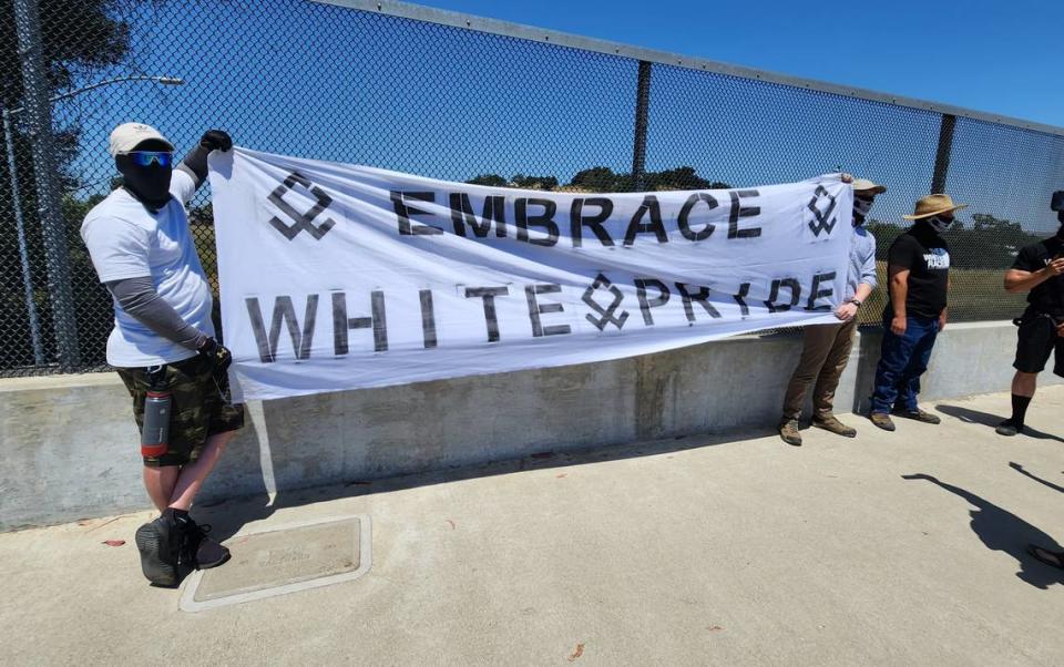 Several men with masks hold up an “Embrace white pride” flag on the Vineyard Drive Highway 101 overpass on Saturday, May 13, 2023.