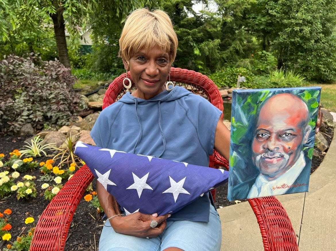 Betty Smith holds a painting of her late husband, Mark M. Smith, who died last summer from COVID at the age of 88. She also holds a flag representing his military service. Smith and the African American Arts Festival will hold a one-mile walk on Saturday morning in memory of those lost to COVID.