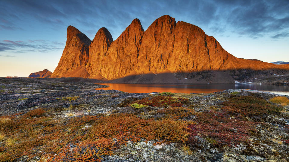     Sunrise at Scoresby Sund shows a large rocky mountain outcrop bathed in golden light. 