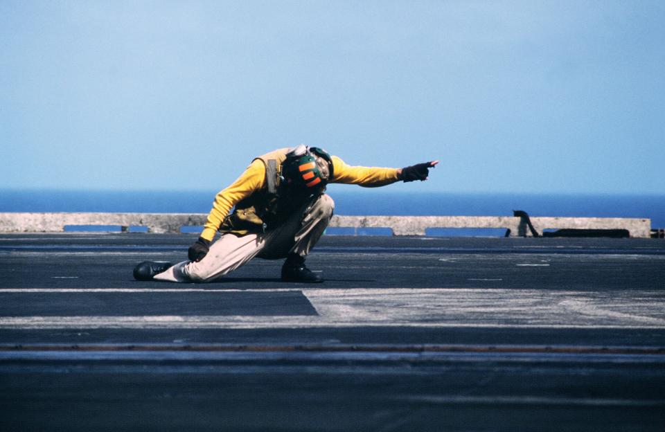 A flight deck crewman signals an aircraft for takeoff from the aircraft carrier USS America.