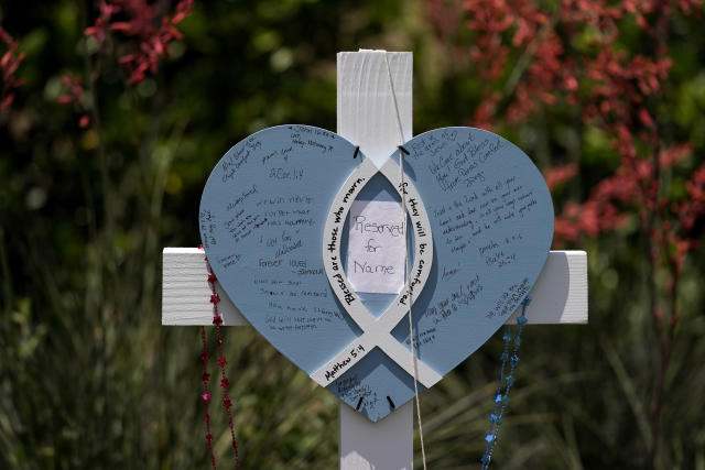 A cross with a heart shape constructed onto it shows messages left by visitors along with a handwritten note that read's "Reserved For Name", at a makeshift memorial by the mall where several people were killed, Monday, May 8, 2023, in Allen, Texas. (AP Photo/Tony Gutierrez)