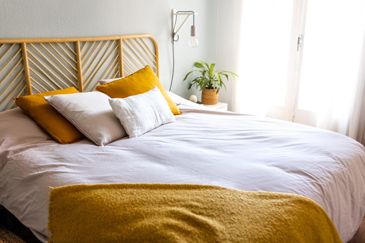 Light and airy cozy bedroom with bed, lamps, cushions and plant. No people. Home interior concept.