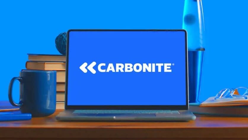  A laptop with the Carbonite logo on screen sitting on a desk in front of a blue wall. 