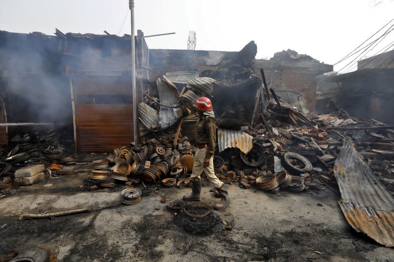 A firefighter walks past damaged shops at a tyre market after they were set on fire by a mob in a riot affected area after clashes erupted between people demonstrating for and against a new citizenship law in New Delhi