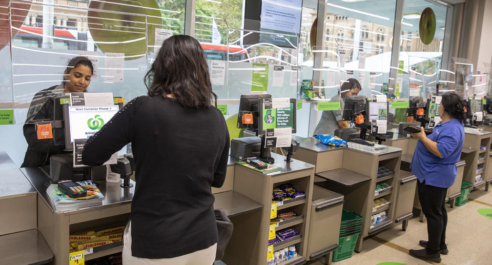 Woolworths shoppers standing in front of checkouts that have plexiglass screens installed to protect staff.