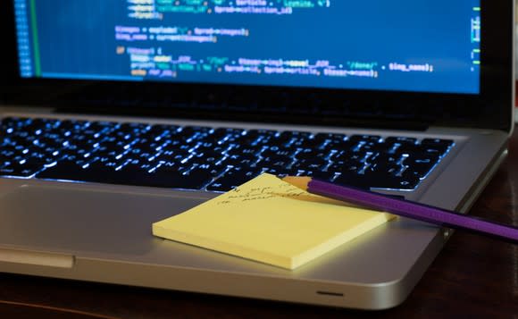 An open laptop with what looks like computer language shown on its screen, with yellow Post-it notes sitting on the laptop and a purple pencil on the notes.