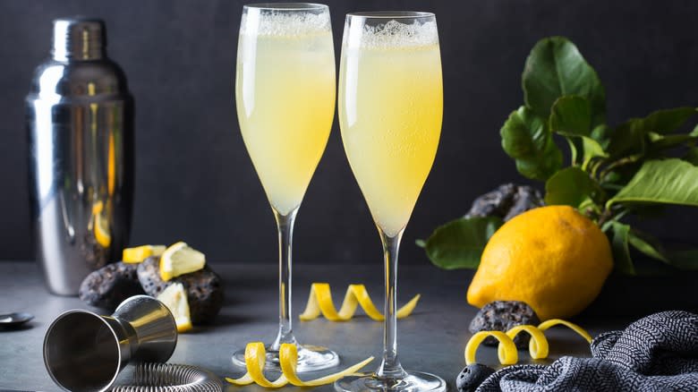 Two French 75 cocktails in flute glasses next to lemon and shaker