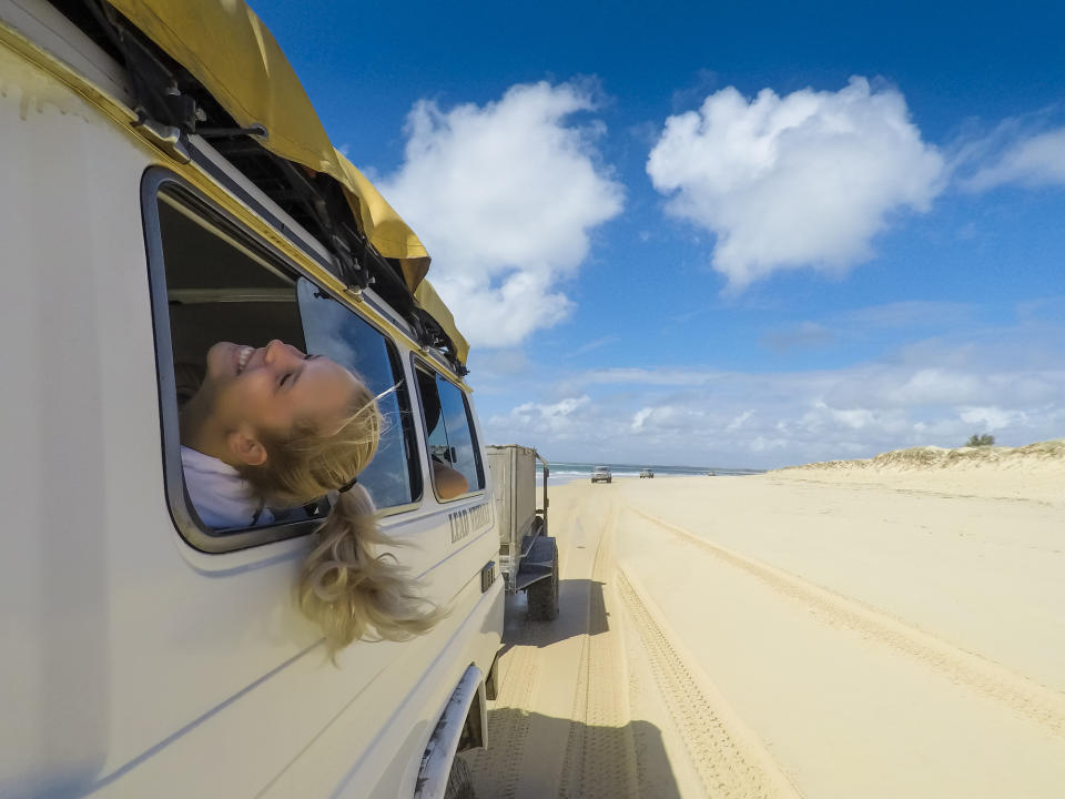 A girl sticks her head out the window as she drives down the beach.