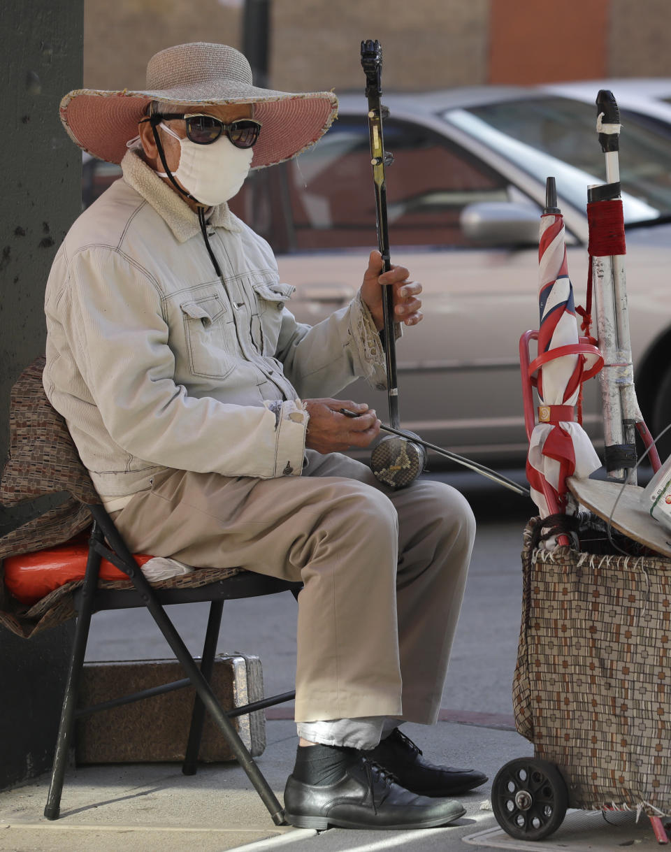 A masked street musician plays in the Chinatown district of San Francisco, Friday, Jan. 31, 2020. As China grapples with the growing coronavirus outbreak, Chinese people in California are encountering a cultural disconnect as they brace for a possible spread of the virus in their adopted homeland. (AP Photo/Ben Margot)