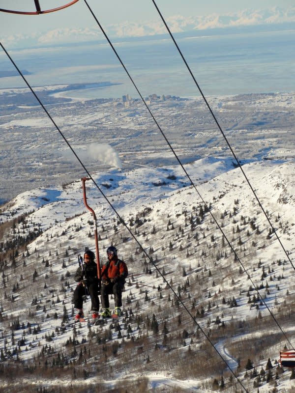 Skiers ride a chairlift at Arctic Valley Ski Area with Anchorage, Alaska in the background<p>Courtesy: Arctic Valley Ski Area</p>