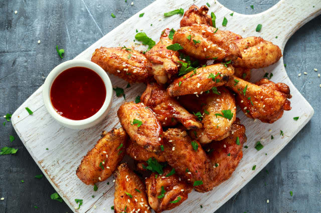 Baked chicken wings with sesame seeds and sweet chili sauce on white wooden board.