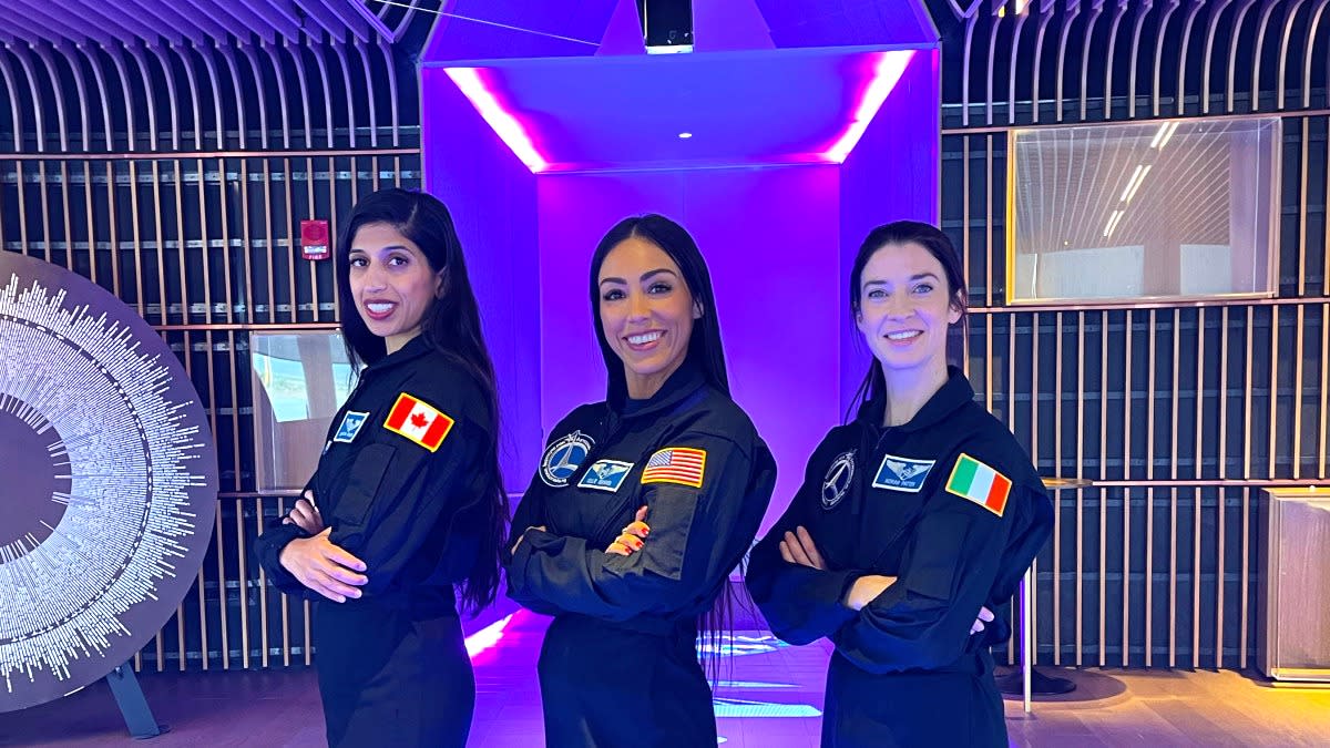  Three astronauts standing in a row in flight suits, smiling with their hands crossed. 